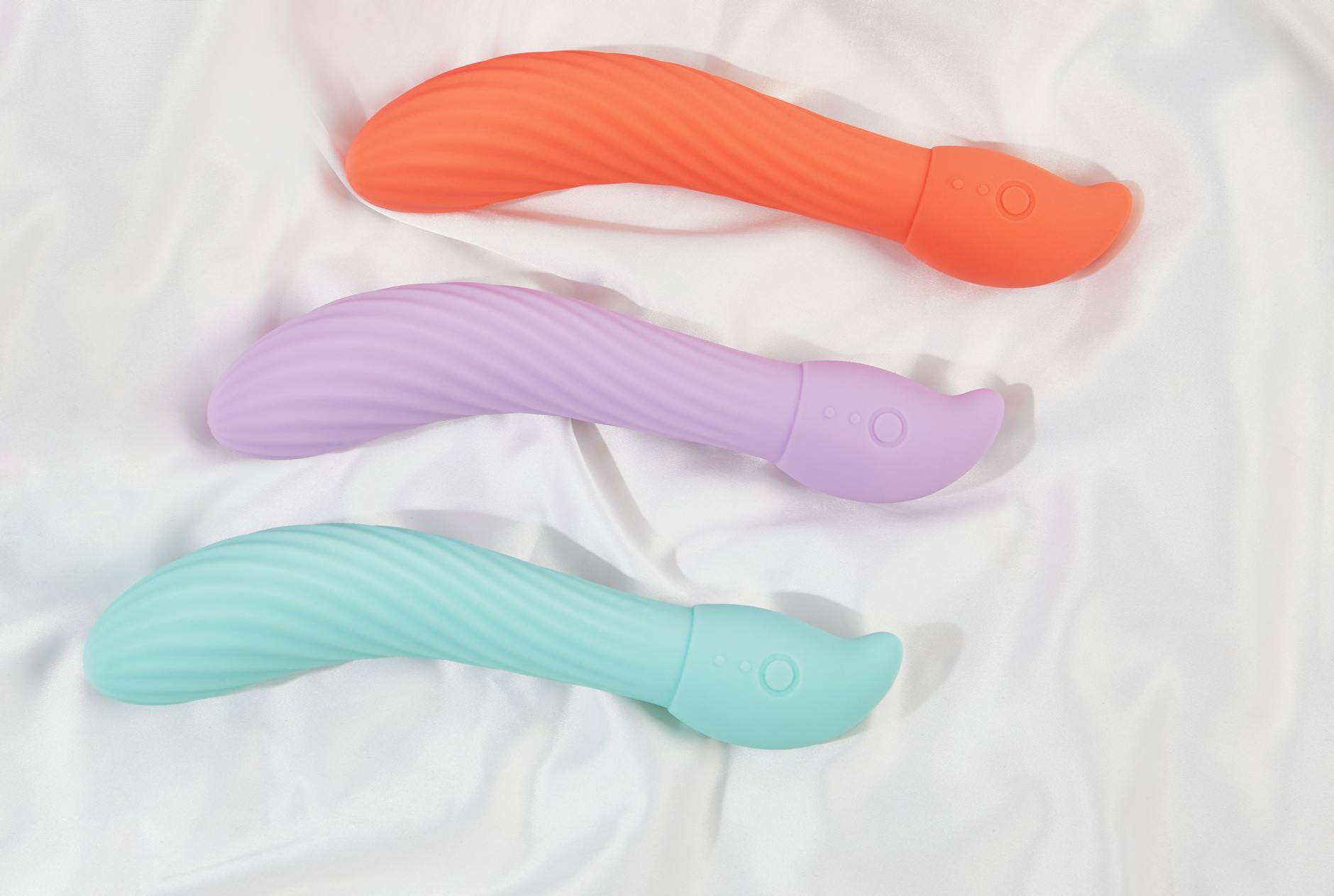 Three colorful vibrators arranged on white fabric, showing smooth texture and design variety.