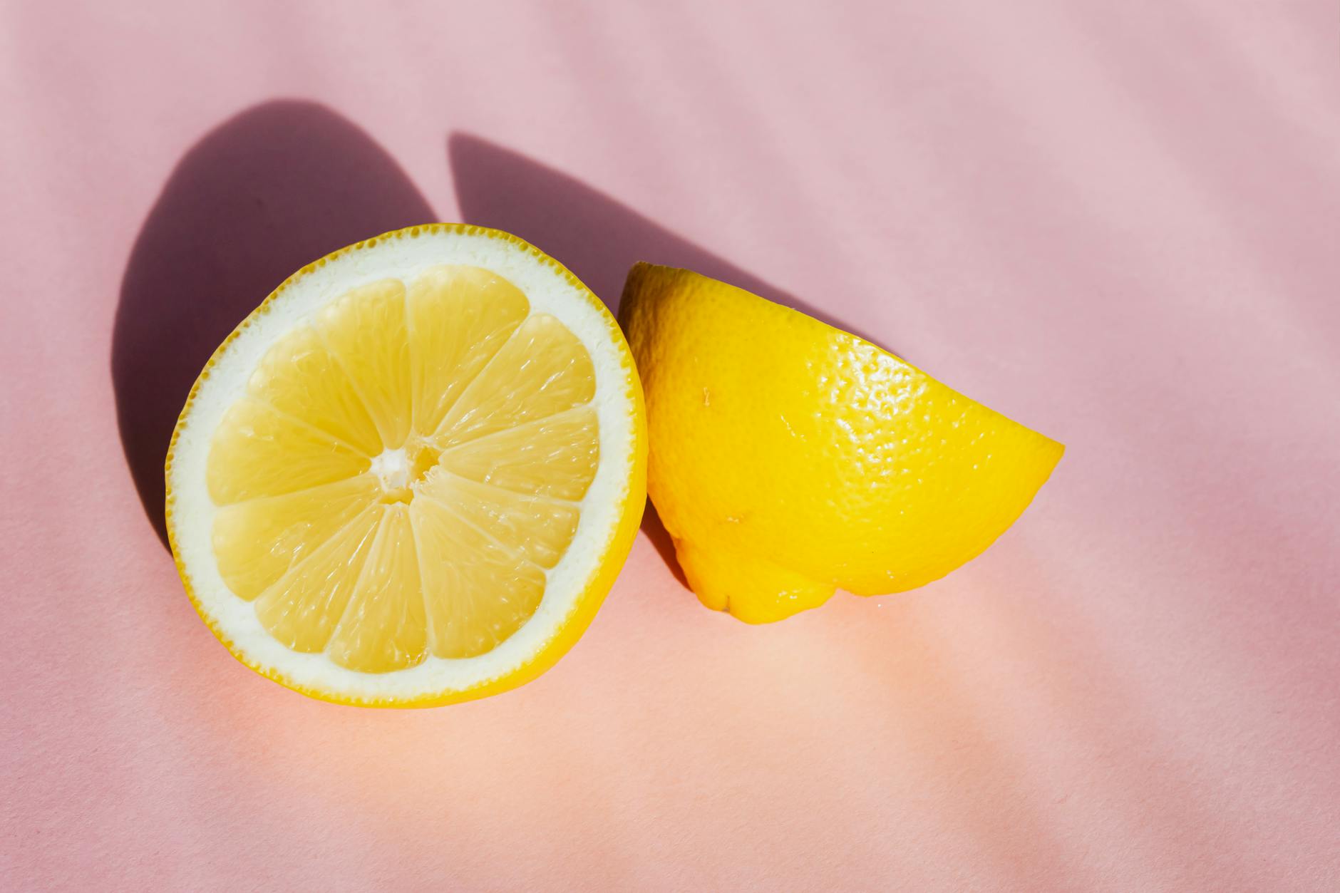 Fresh lemon halves arranged on pink background in natural sunlight