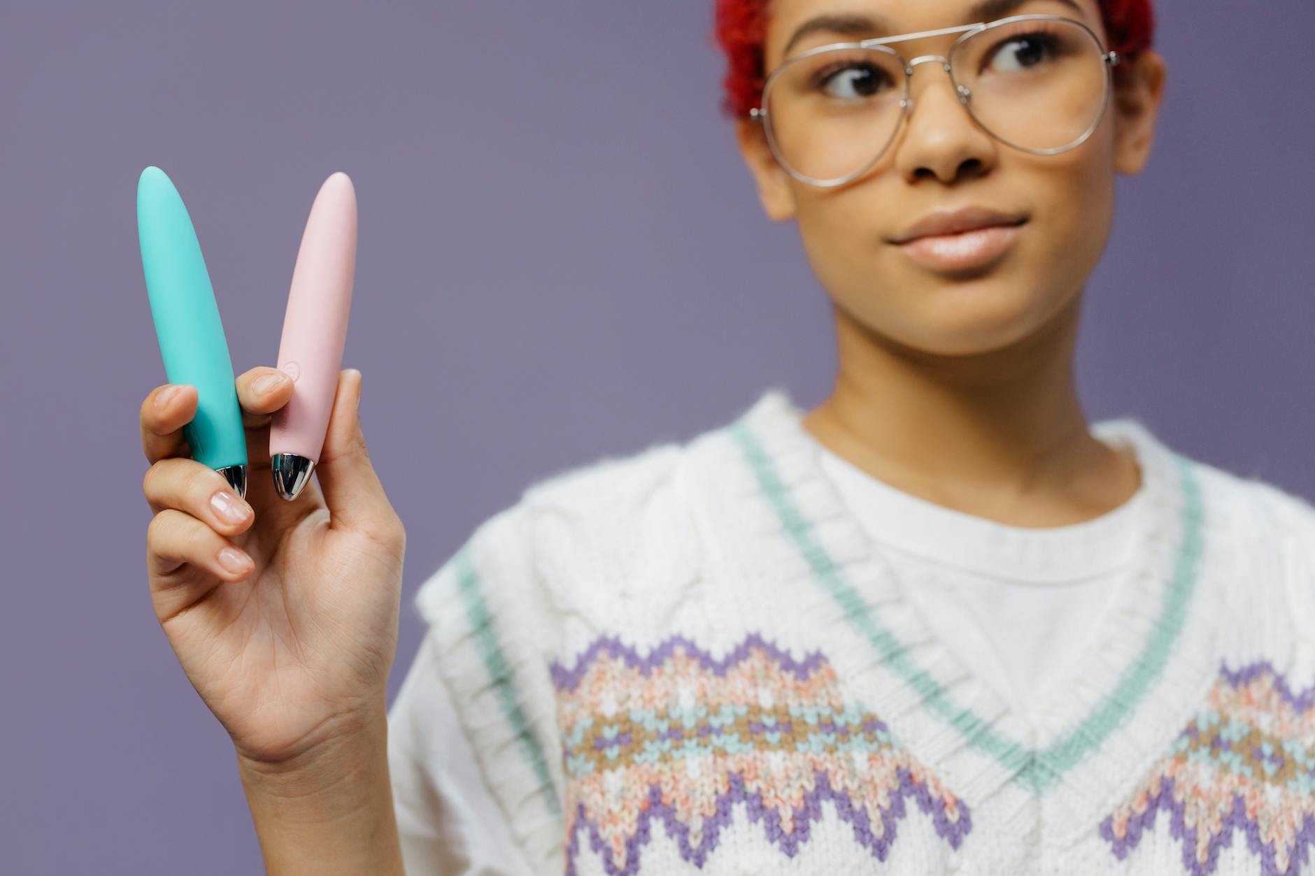 A person holding colorful vibrators against a purple background, showcasing options for pleasure exploration.