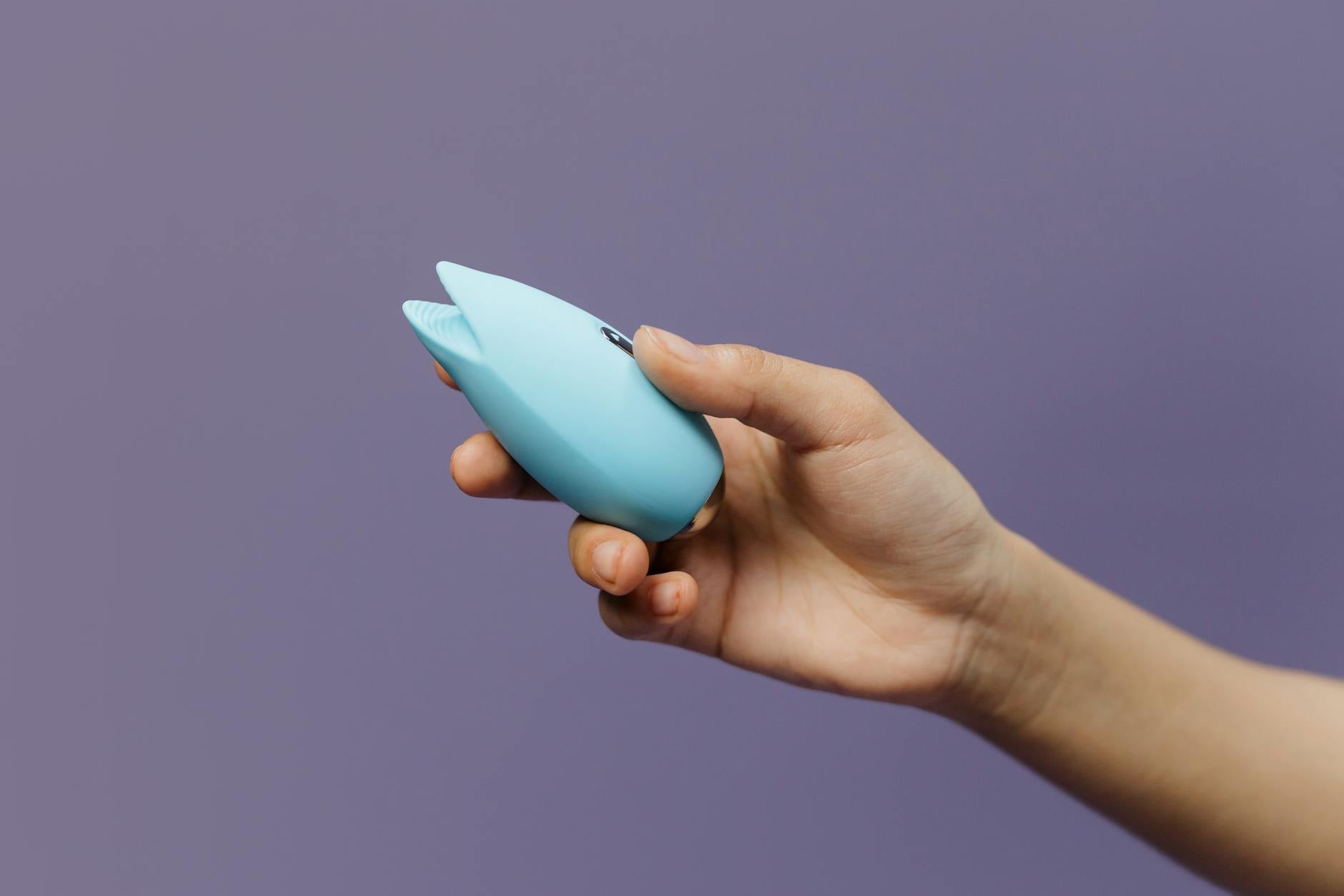 A silicone clitoral vibrator held in hand against a purple background, symbolizing self-pleasure and bodily reconnection.