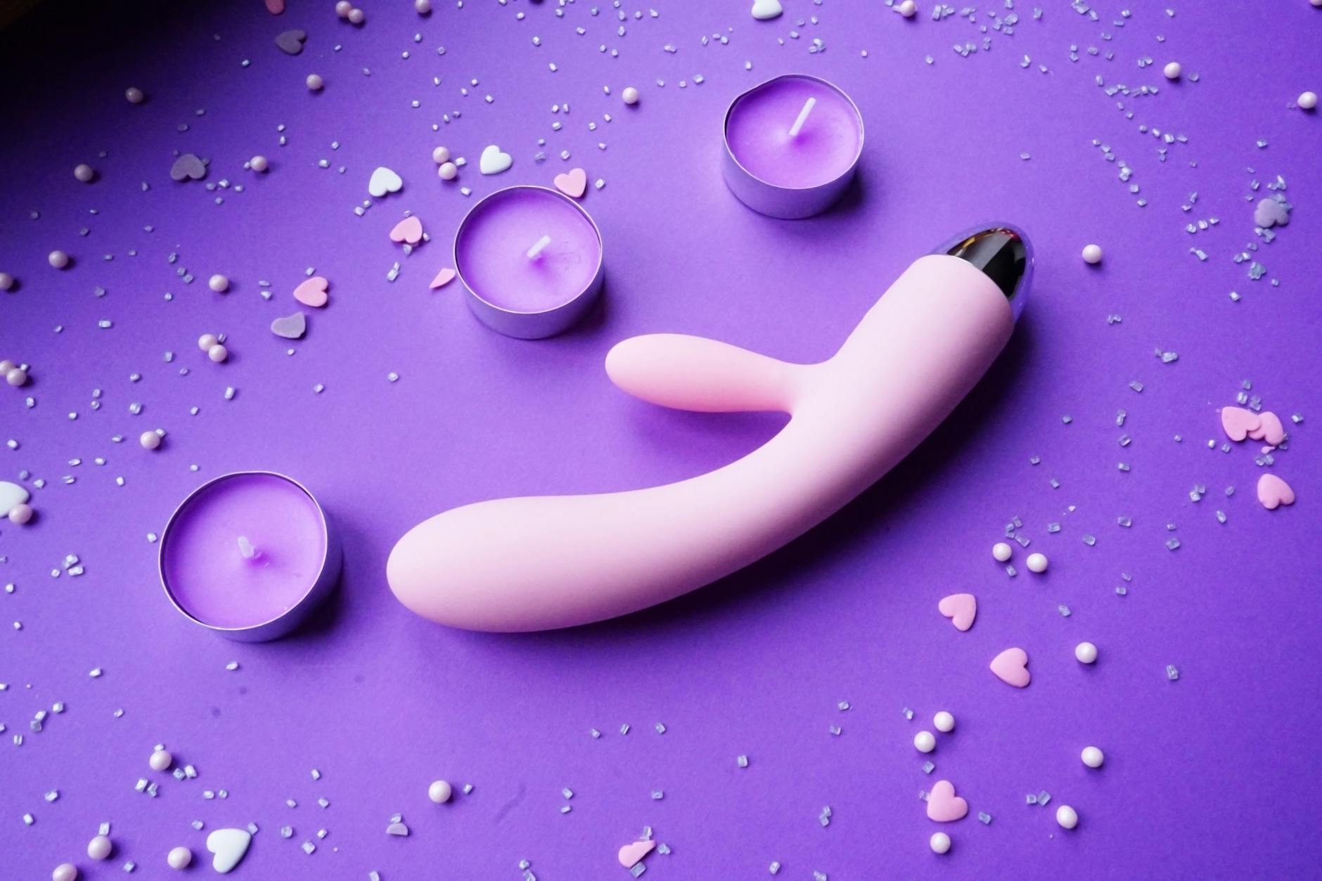 Pink lemon vibrator surrounded by soft candlelight and rose petals on a romantic surface